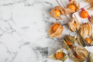Photo of Ripe physalis fruits with dry husk on white marble table, flat lay. Space for text