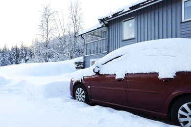 Modern car covered with snow near building on winter day