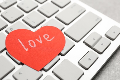 Photo of Paper heart with word LOVE on laptop, closeup