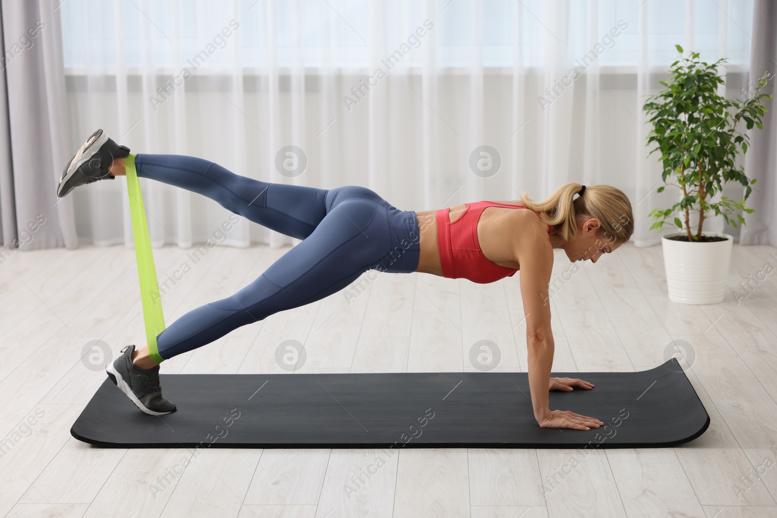 Photo of Athletic woman doing exercise with fitness elastic band on mat at home