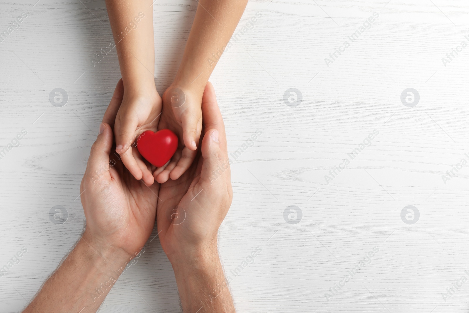 Photo of Family holding small red heart in hands on wooden background