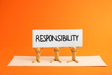 Photo of Three plasticine human figures holding card with word Responsibility on orange background