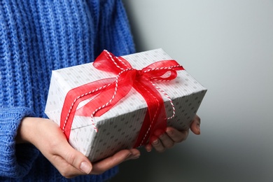 Woman holding white Christmas gift box on grey background, closeup