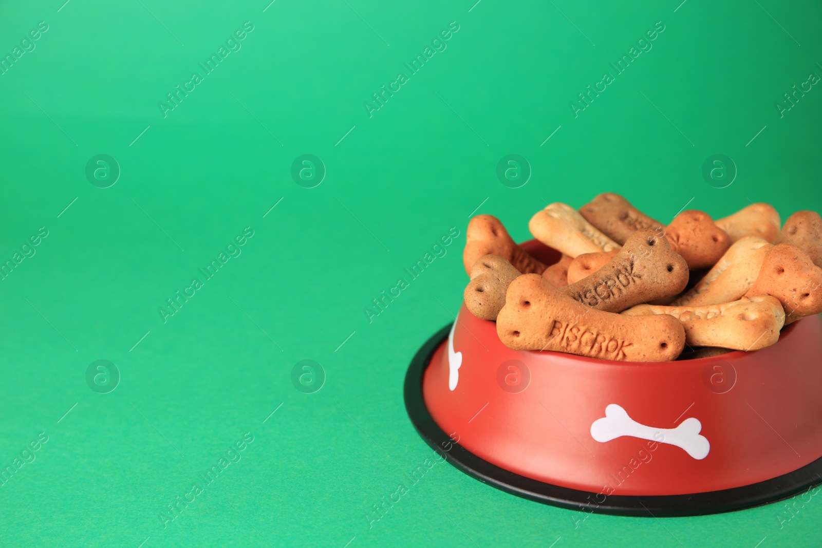 Photo of Bone shaped dog cookies in feeding bowl on green background, space for text