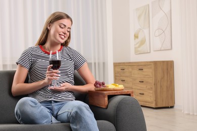 Woman holding glass of wine at home, space for text. Snacks on sofa armrest wooden table