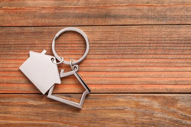 Photo of Metal keychain in shape of houses on wooden table, top view. Space for text