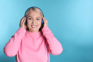 Photo of Mature woman enjoying music in headphones on color background. Space for text