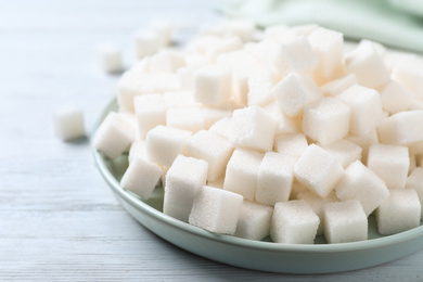 Photo of Refined sugar cubes on white wooden table, closeup