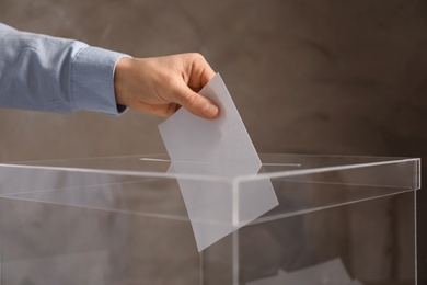 Photo of Man putting his vote into ballot box on color background, closeup