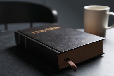 Photo of Hardcover Bible on black table indoors, closeup. Religious book