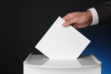 Photo of Man putting his vote into ballot box on dark blue background, closeup