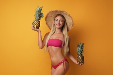 Pretty young woman wearing stylish bikini with pineapples on orange background