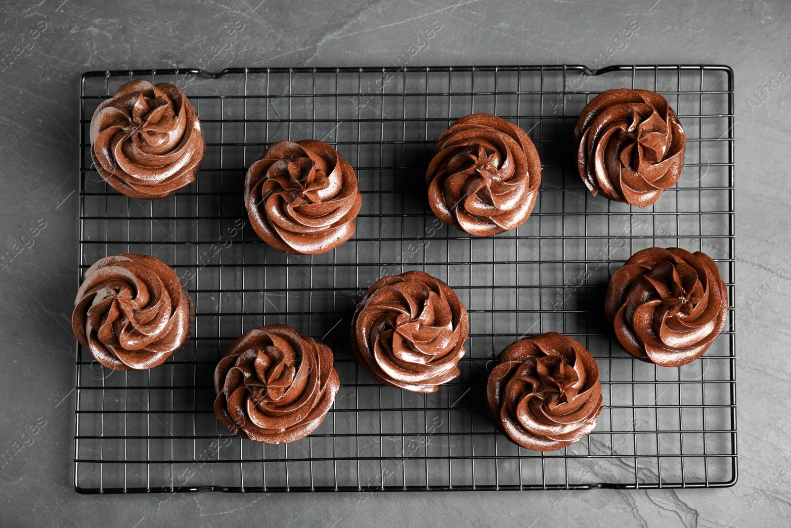 Photo of Cooling rack with delicious chocolate cupcakes on black table, top view