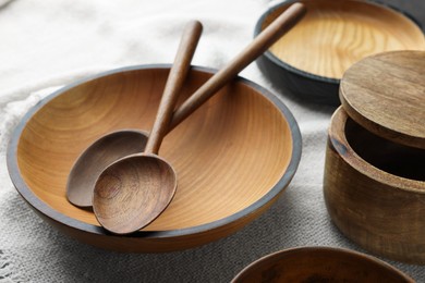Photo of Stylish wooden dishware and spoons on white towel, closeup