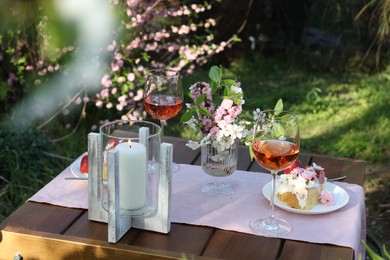 Vase with spring flowers, wine and cake on table served for romantic date in garden