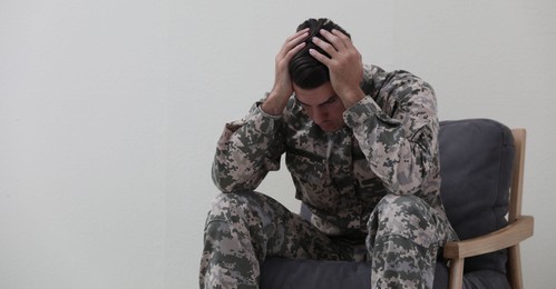 Stressed military officer sitting in armchair on white background. Space for text