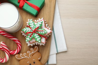 Decorated Christmas cookies and glass of milk on wooden table, top view