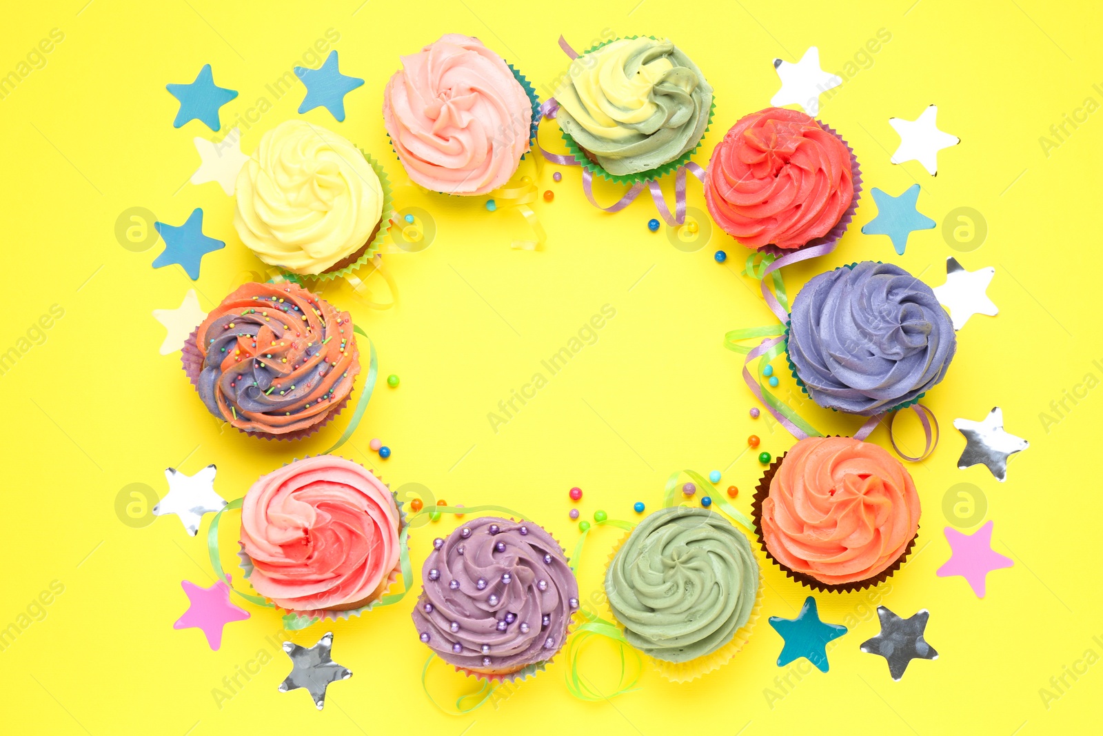 Photo of Delicious cupcakes with bright cream and party decor on yellow background, flat lay. Space for text