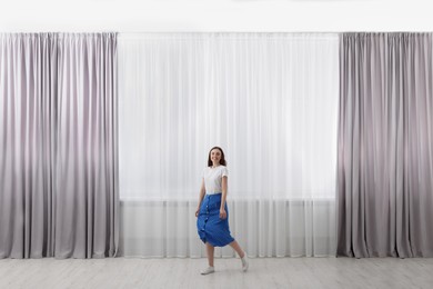 Photo of Woman standing near window with stylish curtains at home