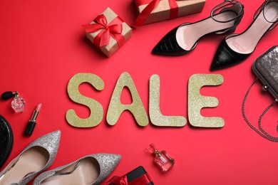 Photo of Word Sale made of golden letters near gift boxes, women's shoes and accessories on red background, flat lay. Black Friday