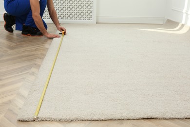 Photo of Worker with measuring tape installing new carpet indoors, closeup