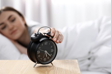 Young woman turning off alarm clock at home in morning, focus on hand. Space for text