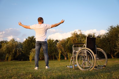 Photo of Man standing near wheelchair outdoors on sunny day, back view. Healing miracle