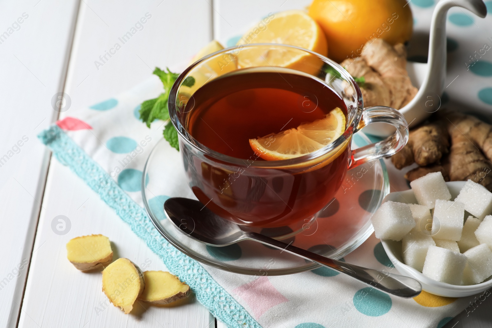 Photo of Cup of delicious ginger tea, sugar cubes and lemons on white wooden table