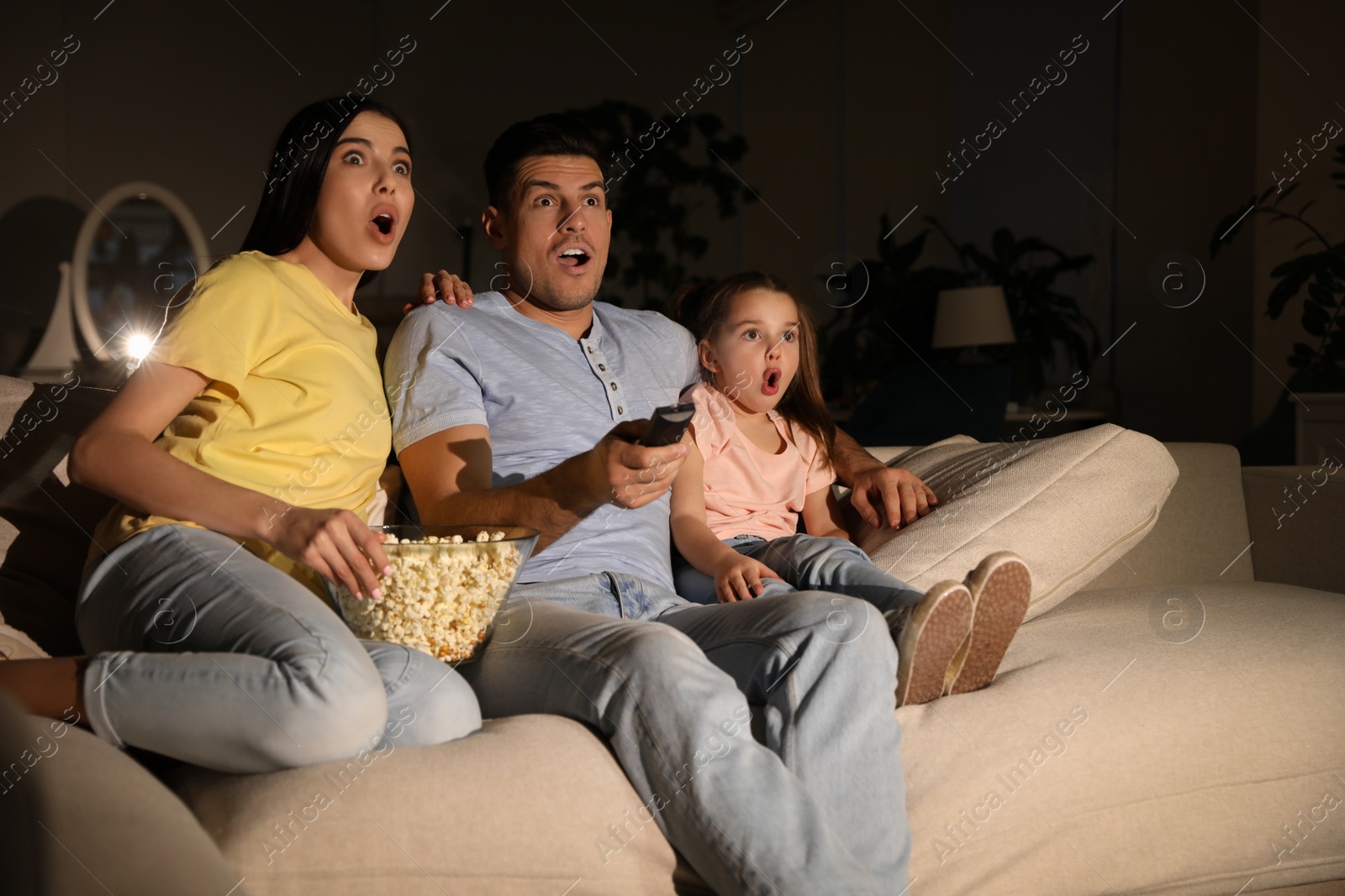 Photo of Family watching movie with popcorn on sofa at night