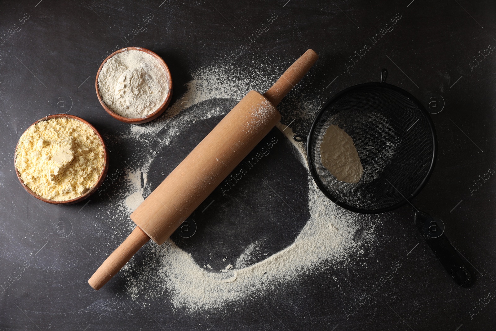 Photo of Scattered flour, rolling pin and sieve on black table, flat lay