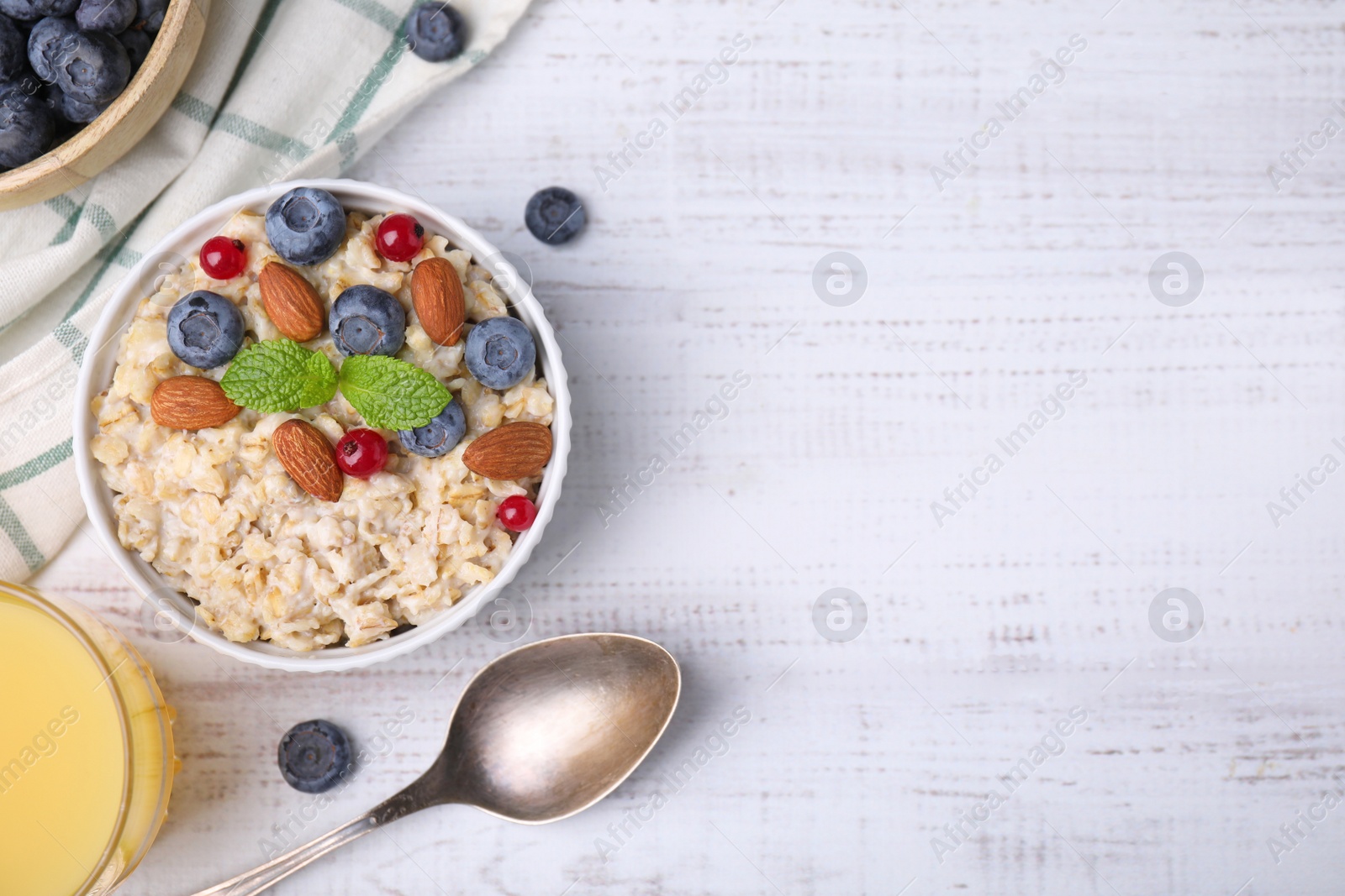 Photo of Oatmeal served with berries. almonds and mint on white table, flat lay. Space for text