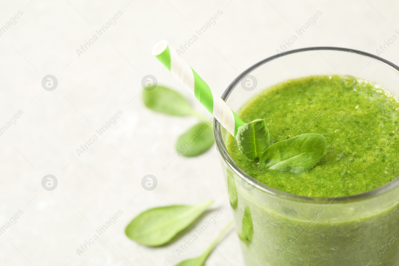 Photo of Green juice and fresh spinach leaves on light grey table, closeup. Space for text