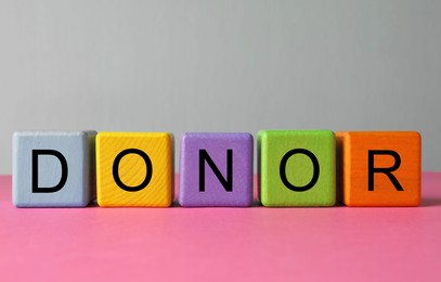 Word Donor made of colorful wooden cubes on pink table