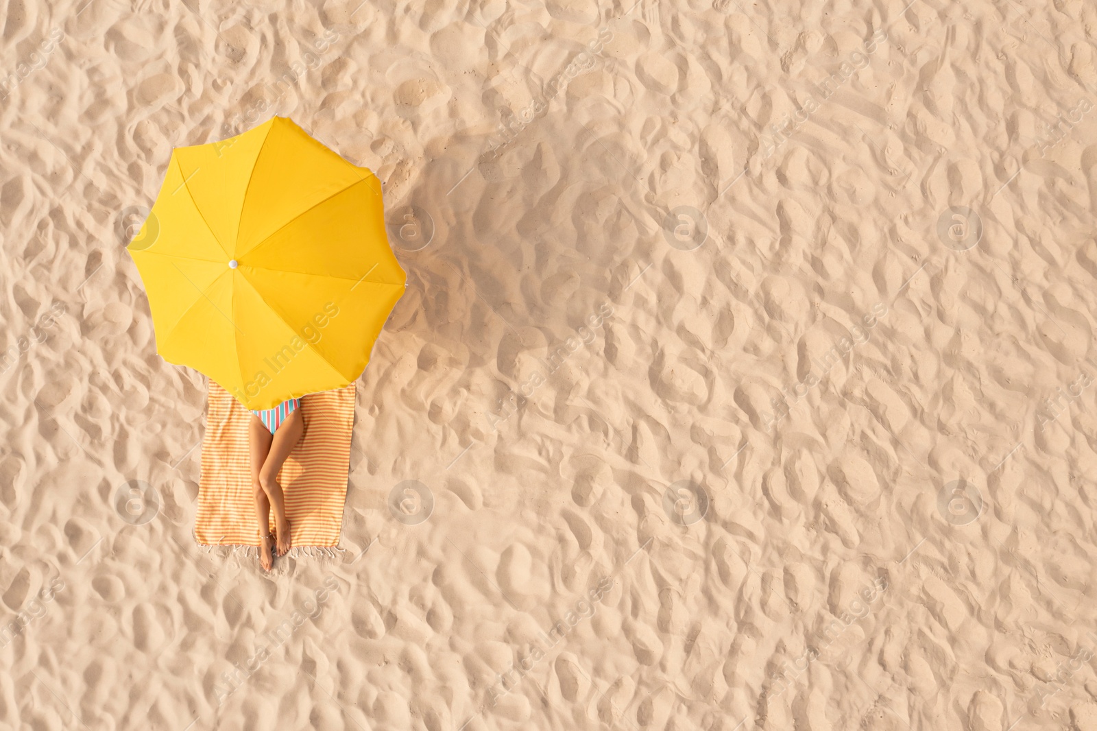 Image of Woman resting under yellow beach umbrella at sandy coast, aerial view. Space for text