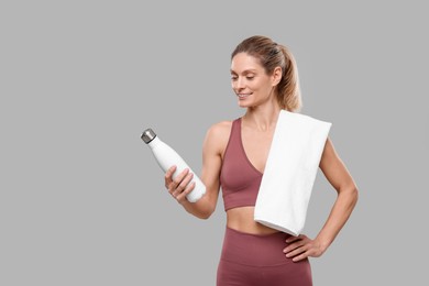 Sportswoman with thermo bottle and white towel on grey background, space for text