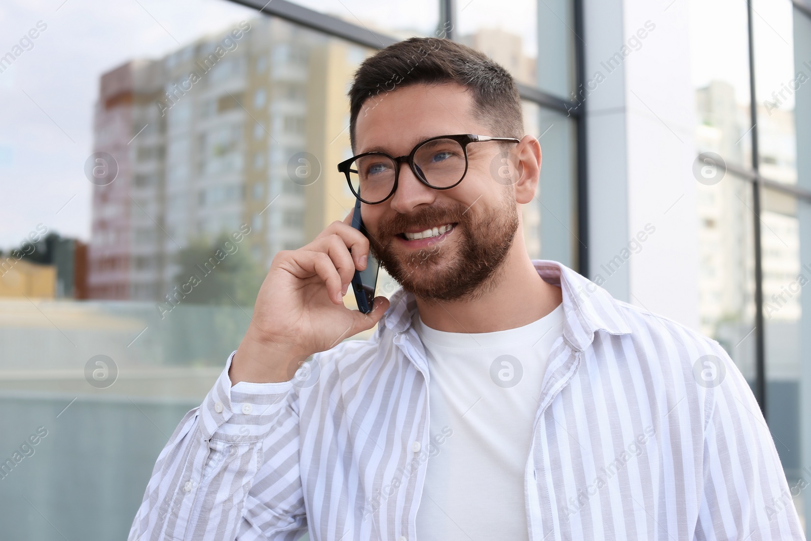 Photo of Handsome bearded man in glasses talking on phone outdoors