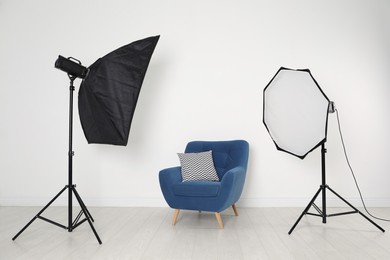 Photo of Comfortable armchair and professional lighting equipment in photo studio