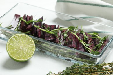 Raw black carrot with sprouts and lime on white table, closeup