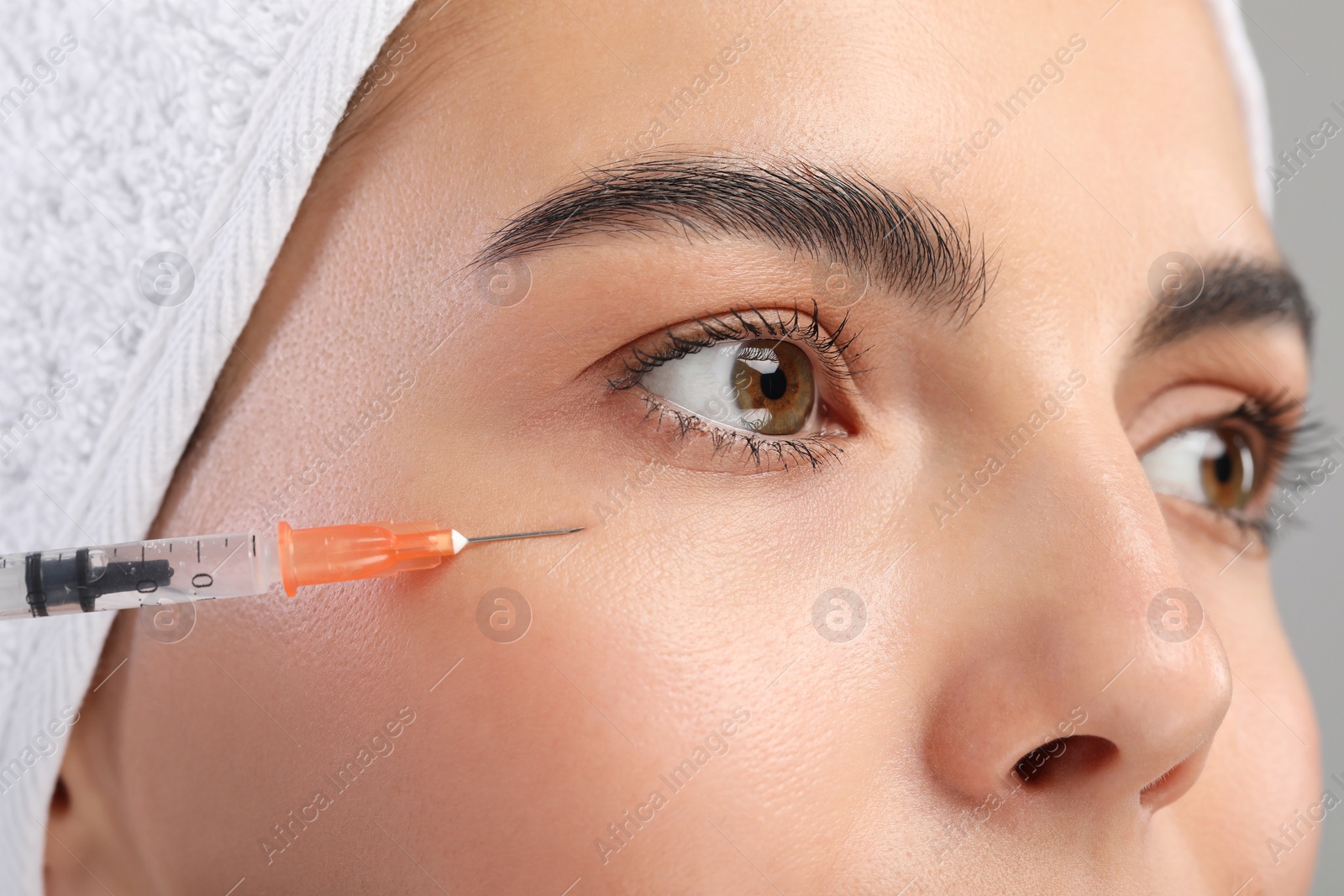 Photo of Young woman getting facial injection on light grey background, closeup. Cosmetic surgery