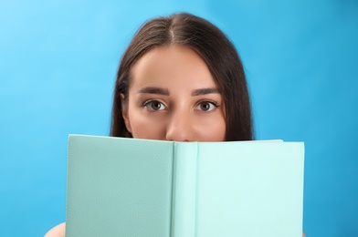 Beautiful young woman reading book on light blue background