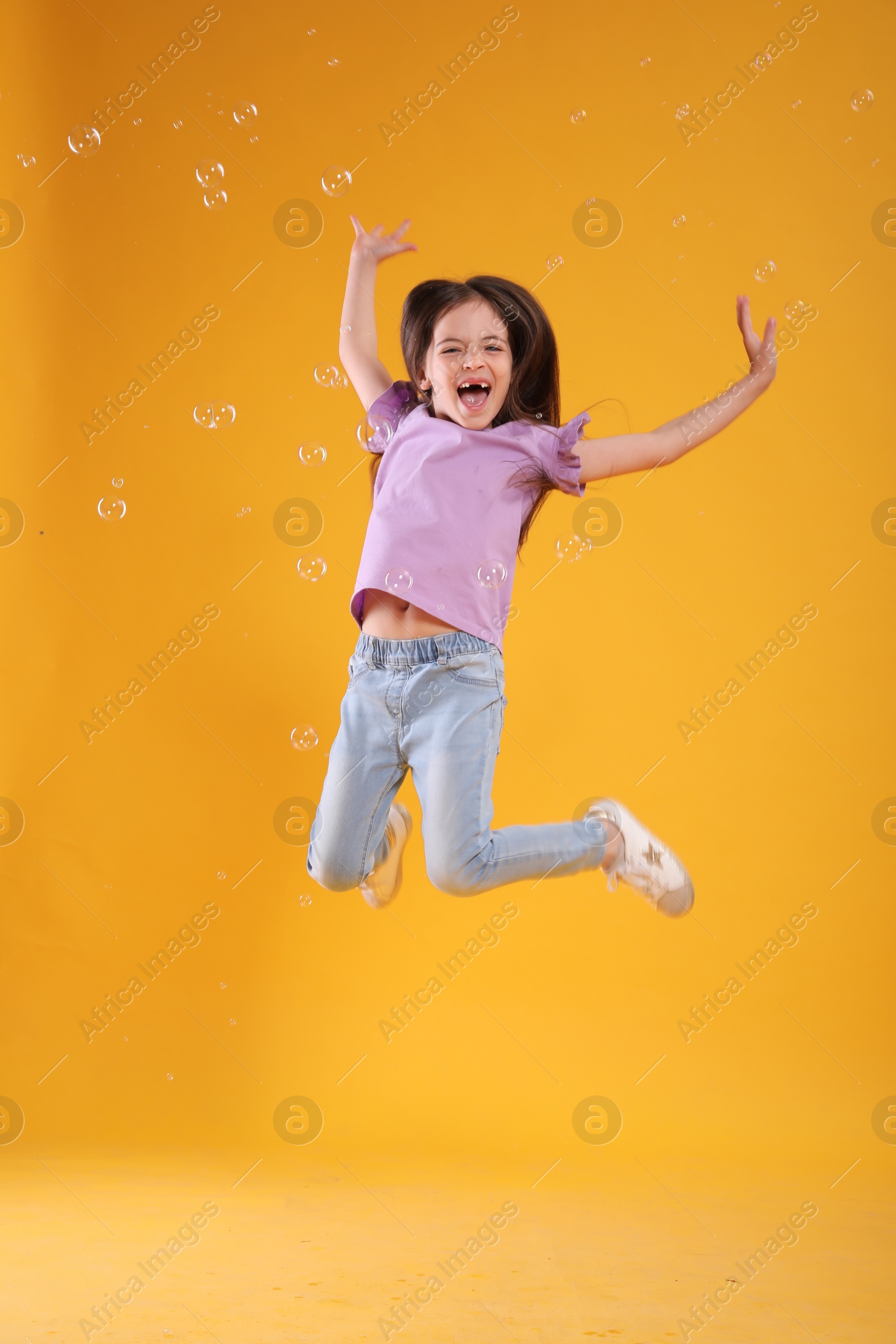 Photo of Little girl having fun with soap bubbles on yellow background