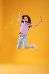 Little girl having fun with soap bubbles on yellow background