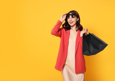 Photo of Beautiful young woman with paper shopping bags on yellow background. Space for text