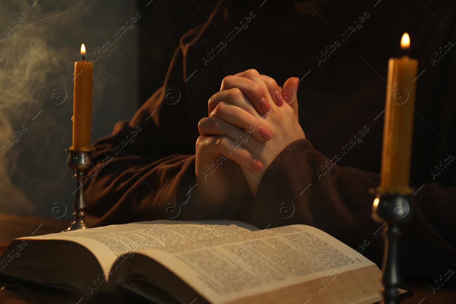 Photo of Woman praying at table with burning candles and Bible, closeup