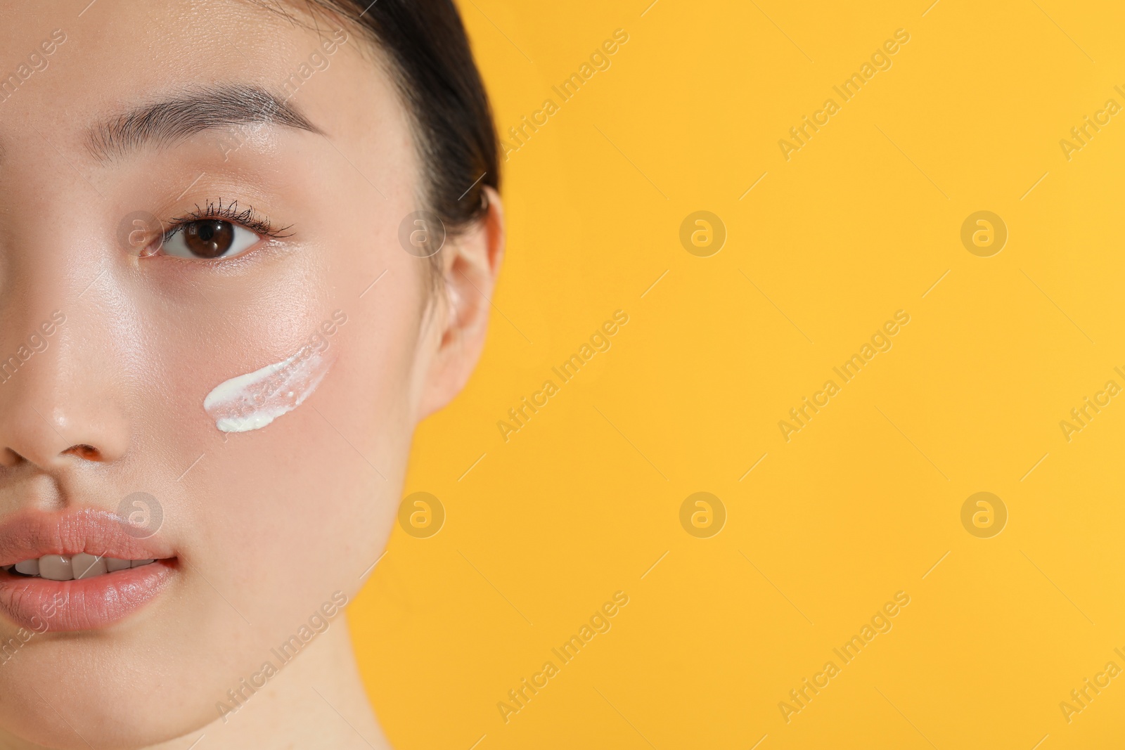 Photo of Beautiful young woman with sun protection cream on her face against orange background, closeup. Space for text