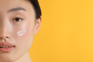 Beautiful young woman with sun protection cream on her face against orange background, closeup. Space for text