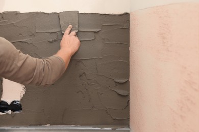 Photo of Worker spreading adhesive mix for installing tile on wall indoors, closeup