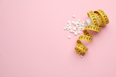 Photo of Jar of weight loss pills and measuring tape on pink background, flat lay. Space for text
