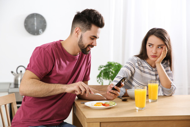 Photo of Young man preferring smartphone over his girlfriend at home