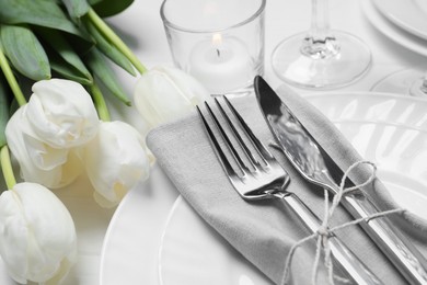 Stylish setting with cutlery, burning candle and tulips on white wooden table, closeup